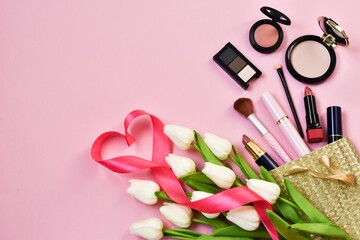 Obraz na płótnie Canvas Make up cosmetics,lipstisks,powder face,mascara,makeup brushes with tulips flowers in gift bag on pink background. Copy space. Flat lay. Festive cosmetic sale.