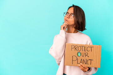 Fototapeta na wymiar Young hispanic mixed race woman holding a protect our planet cardboard looking sideways with doubtful and skeptical expression.