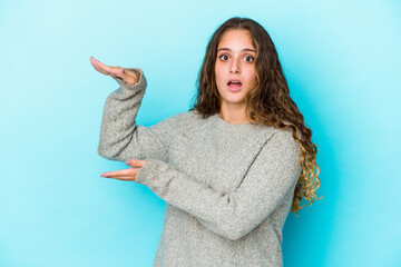 Young caucasian curly hair woman isolated shocked and amazed holding a copy space between hands.