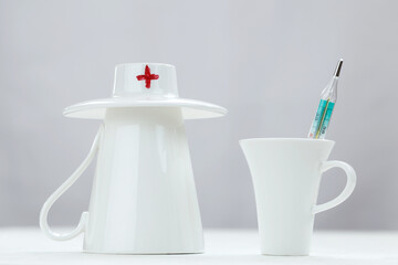 Two white cups - one as a doctor, another one as a patient with thermometer standing together