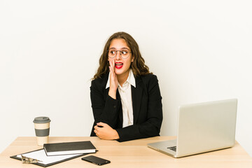 Young caucasian business woman working on her desktop isolated is saying a secret hot braking news and looking aside