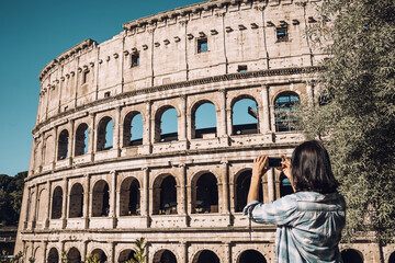 Fototapeta na wymiar Young woman take a picture of Colosseum by smartphone in Rome