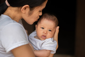 Young Asian mother kissing and holding little daughter in the park, Mother play enjoying with her cute baby girl in outdoor, copy space
