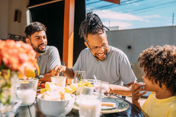 Fototapeta na wymiar Latinx gay couple having breakfast with their curly-haired son
