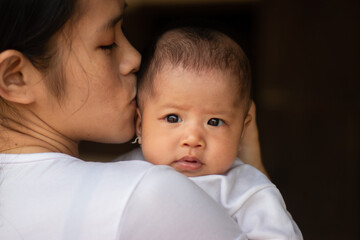Young Asian mother kissing and holding little daughter in the park, Mother play enjoying with her cute baby girl in outdoor, copy space

