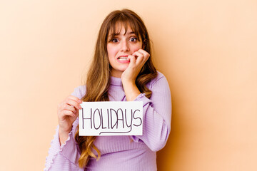 Young caucasian woman holding a Holidays placard isolated biting fingernails, nervous and very anxious.