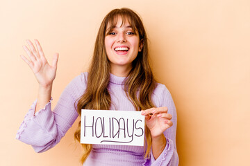 Fototapeta na wymiar Young caucasian woman holding a Holidays placard isolated receiving a pleasant surprise, excited and raising hands.