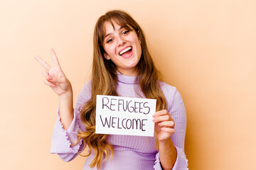 Fototapeta na wymiar Young caucasian woman holding a Refugees welcome placard isolated joyful and carefree showing a peace symbol with fingers.