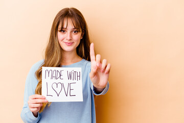 Fototapeta na wymiar Young caucasian woman holding a made with love placard isolated showing number one with finger.