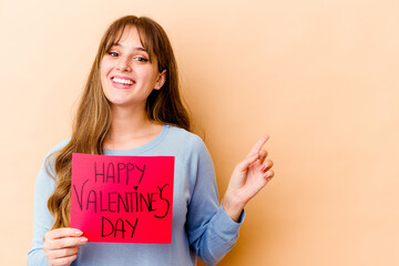 Fototapeta na wymiar Young caucasian woman holding a Happy Valentines day isolated smiling and pointing aside, showing something at blank space.