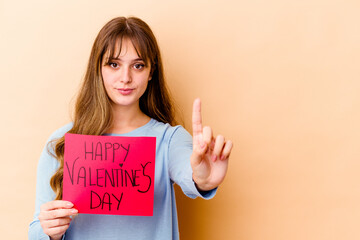 Fototapeta na wymiar Young caucasian woman holding a Happy Valentines day isolated showing number one with finger.