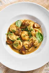 Dumplings Food Restaurant Plate. Dumplings With Creamy Porcini Sauce. White restaurant plate on white table. Rustic restaurant food concept.