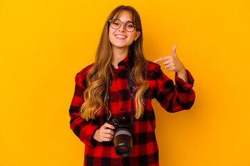 Young photographer caucasian woman isolated on yellow background person pointing by hand to a shirt copy space, proud and confident