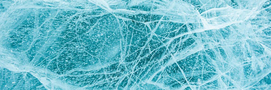 Texture of beautiful blue ice with cracks and air bubbles in the frozen lake. Winter nature background. Lake Baikal, Siberia, Russia. Banner.
