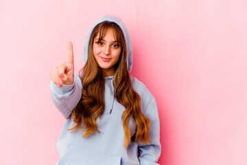 Young caucasian woman with hood isolated on yellow background showing number one with finger.