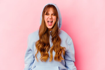 Young caucasian woman with hood isolated on yellow background screaming very angry and aggressive.