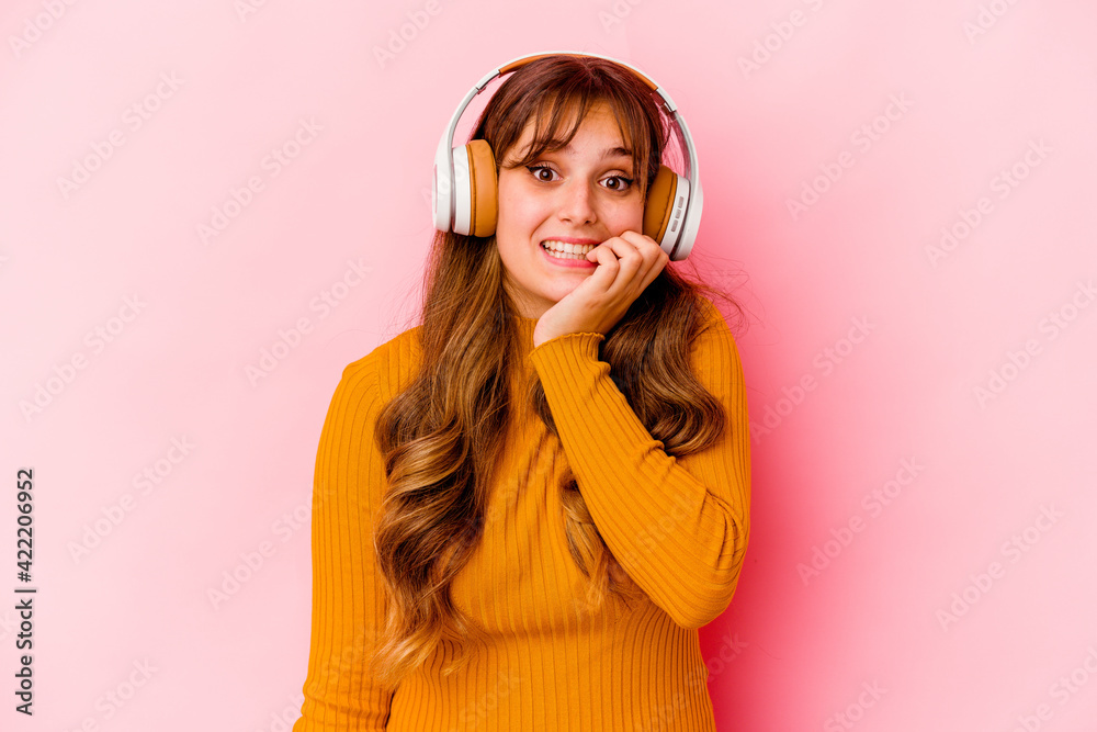 Wall mural Young caucasian woman listening music with headphones isolated biting fingernails, nervous and very anxious.