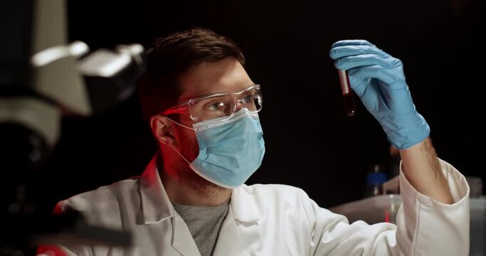 Doctor Examing Blood Test in Flusk in Laboratory. Laboratory Worker with Blood Sample. Covid Test. Blood Test. Man Working wearing Medical Mask, Glasses and Gloves.