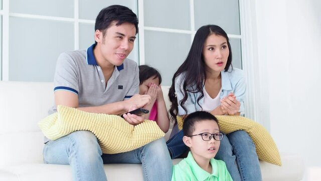 Happy asian family watching scary movie at home.