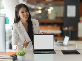 Fototapeta premium Businesswoman in white suit presenting digital tablet and pointing to mock up screen
