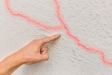 Male construction worker hand points cracks on white broken wall background. Renovation concept