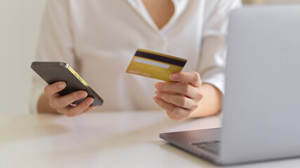 Female hands holding smartphone and credit card to online payment on workspace