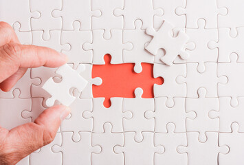 Top view flat lay of hand-holding last piece white paper jigsaw puzzle game last pieces put to place for solve problem complete mission, studio shot on a pink background, quiz calculation concept