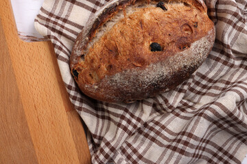 Rustic whole grain artisan bread loaf with cranberry raisin dry fruit nuts wrapped in checkers cloth with wooden chopping board over table top flat lay view