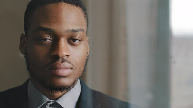 Portrait of serious focused pensive dark-skinned business man afro american investor looking out window in office, making decision pondering proposal, turns to camera waves nods his head in agreement