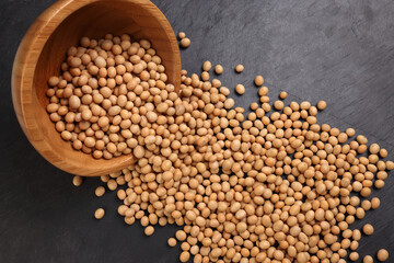 Soyabeans soya beans in wooden bowl flowing over black slate stone background copy text space flat lay top view