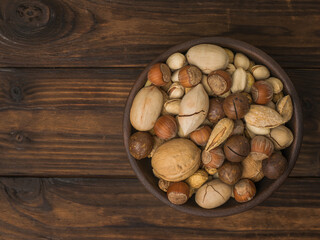 A mixture of a large number of different nuts in a clay cup on a wooden table.