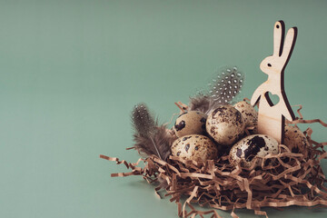 Easter nest made of hay with quail eggs, bunny and feathers on a blue background, close-up. Easter composition in pastel colors. Natural Easter background, creative layout