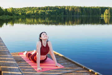 Fototapeta na wymiar girl doing yoga on wooden pier by lake in summer