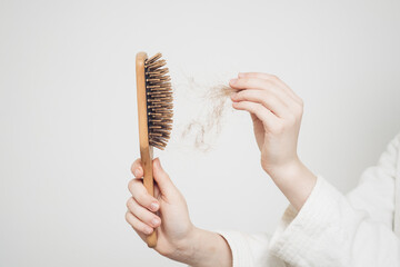 woman removes a bun of hair with a wooden comb on a light background health problems loss - obrazy, fototapety, plakaty