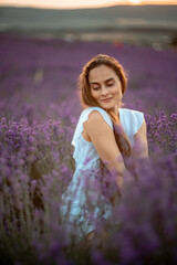 A beautiful girl in a white dress and loose hair on a lavender field. Beautiful woman in a lavender field at sunset. Soft Focus