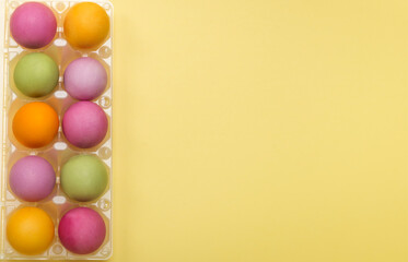 flat laying, colored easter eggs in a container on a yellow background with a copy of the space
