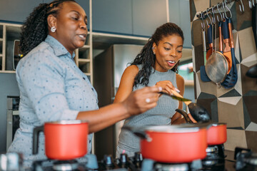curly haired senior woman cooking happily at home with her daughter