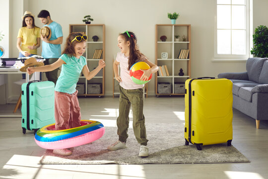 Happy Children Packing For Holiday And Having Fun With Inflatable Toys At Home. Carefree Kids Playing With Beach Ball And Pool Floaty While Mom And Dad Are Getting Ready For Family Travel Vacation