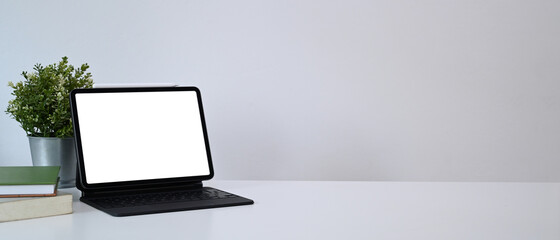 Mock up computer tablet with blank screen, house plant and books on white table. Copy space for products display montage.