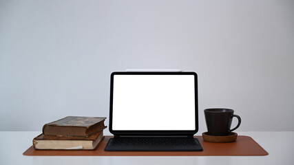 Front view of computer tablet, books and coffee cup on white office desk.