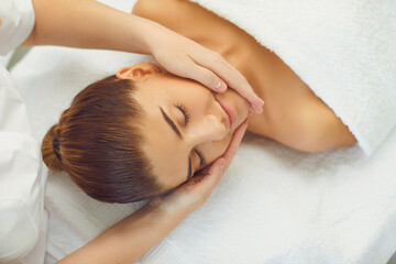 Fototapeta na wymiar Woman enjoying procedure of facial massage from cosmetologist