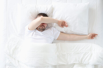 Obraz na płótnie Canvas An adult man sleeps in bedroom on large bed