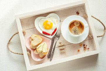 Father's Day. Breakfast for Dad. On the tray there is a cup of coffee and two plates in the shape of a heart with scrambled eggs and bread and butter. View from above.