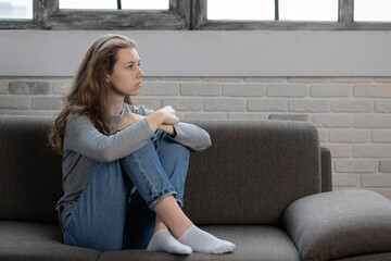 Depressed teenager girl with sad emotions and feelings sitting on the couch at home