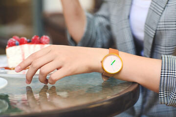 Woman with stylish wrist watch eating cake in cafe
