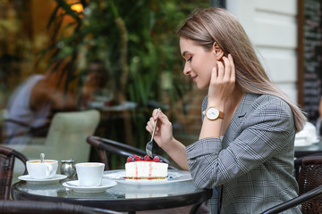 Woman with stylish wrist watch eating cake in cafe