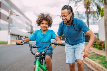 latinx father is teaching her son to ride the bike