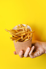 Female hand and box with tasty french fries on color background