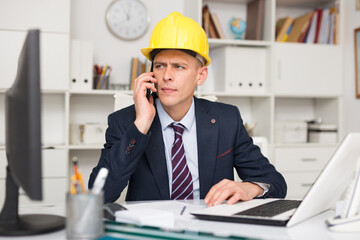 Male engineer sitting in an office is discussing important current work issues with a colleague on the phone