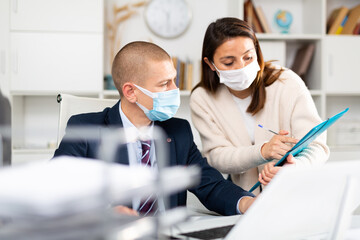 Fototapeta na wymiar Corporate business coleagues businessman and businesswoman in face masks discussing something and working together in modern office